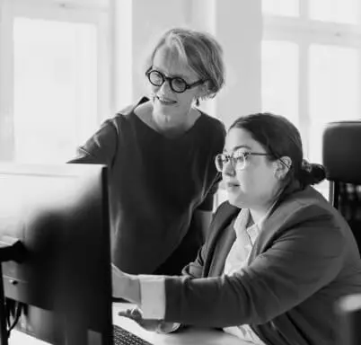 Two colleagues look at a computer monitor; one assists the other.